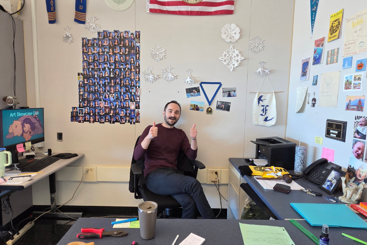 Connor Fenech poses for a picture at his desk, surrounded by many pictures and student works on the walls. The windows and blinds in his room are kept open to provide a light environment for students.