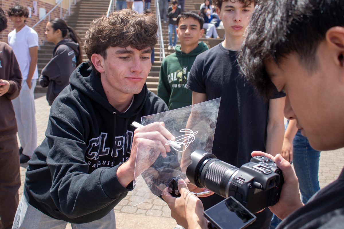 Senior Theo Scherer signs a fiberglass sheet during the Carlmont Commit Day celebration. During the event, a cameraman from Carlmont Associated Student Body (ASB) captured seniors "signing" off for their senior years. "The activities were fun, and I liked the senior sign off," Scherer said.